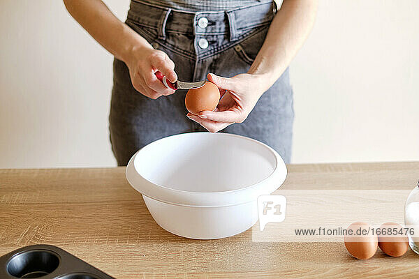 Frau bricht ein Ei mit einem Messer über einem Teller auf  um eine köstliche Mahlzeit zuzubereiten