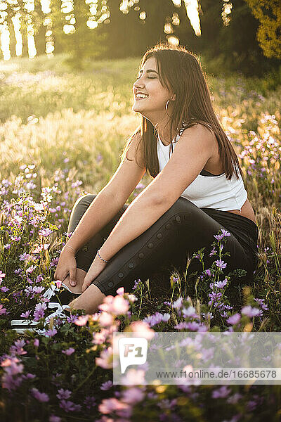 Glücklicher Teenager  der bei Sonnenuntergang auf einem Feld zwischen Blumen lacht