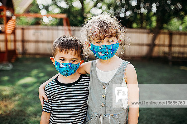Zwei junge Kinder stehen draußen und tragen selbstgemachte Masken