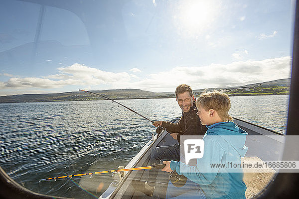 Man fishing with cheerful boy on boat in sea
