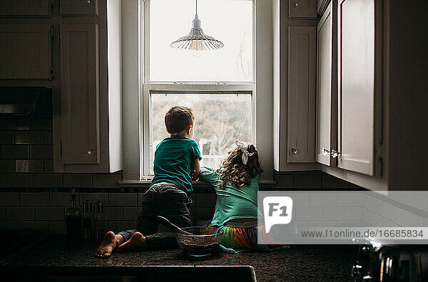 Junge und Mädchen starren an einem regnerischen Tag aus dem Küchenfenster