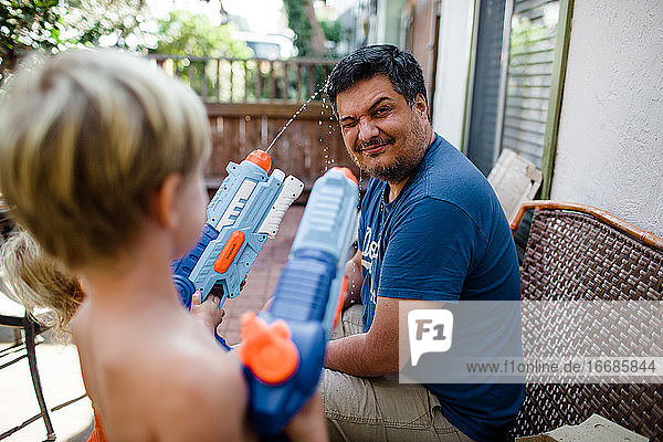Neffen schießen mit Wasserpistolen auf Onkel im Vorgarten