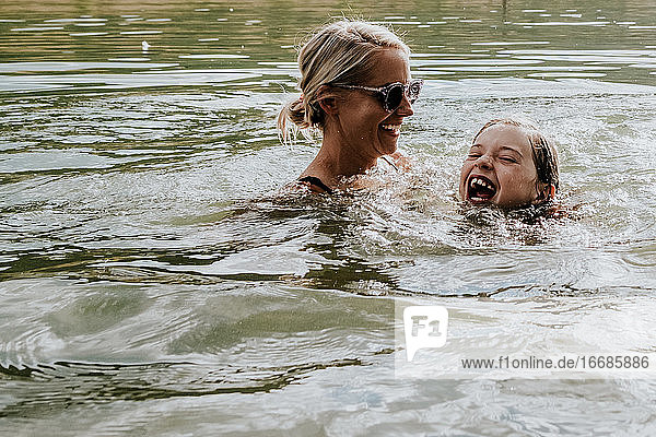 Mom and young daughter joyfully swimming in a lake on a sunny day