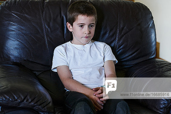 Kind sitzt auf einer dunklen Couch und sieht fern