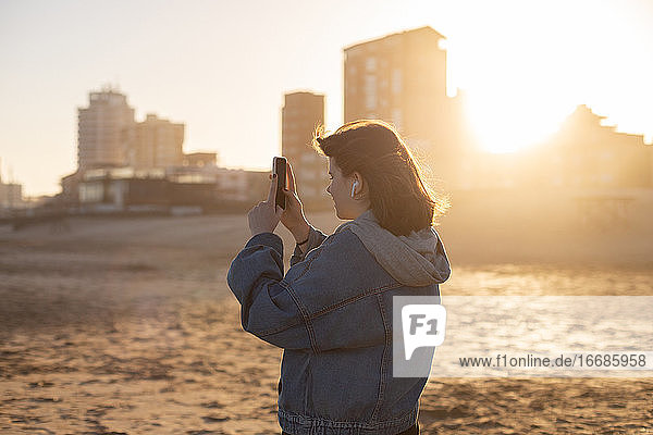 Mädchen fotografiert mit dem Handy den Sonnenuntergang am Strand des Atlantischen Ozeans
