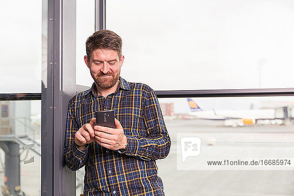 Gut gelaunter Mann mit Smartphone auf dem Flughafen