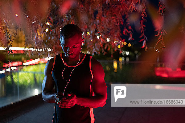 Schwarzer Sportler mit Smartphone unter einem Baum