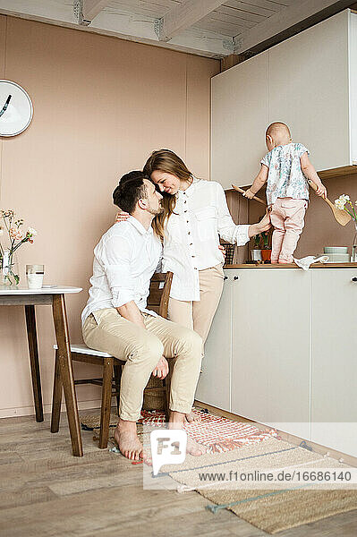 Hübsche dreiköpfige Familie in der Küche. Die Mutter umarmt den Vater und schaut ihn liebevoll an.