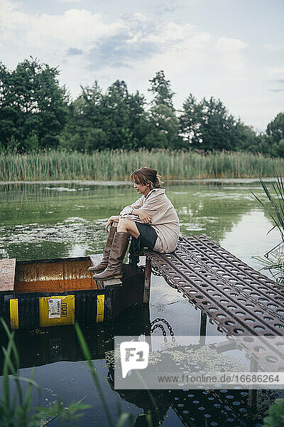 Frau sitzt auf einem Holzsteg in der Nähe des Bootes