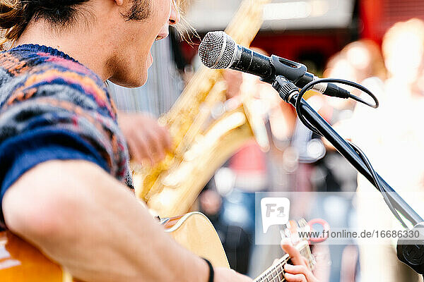 Selective focus on a face of a man singing and playing a guitar in the street