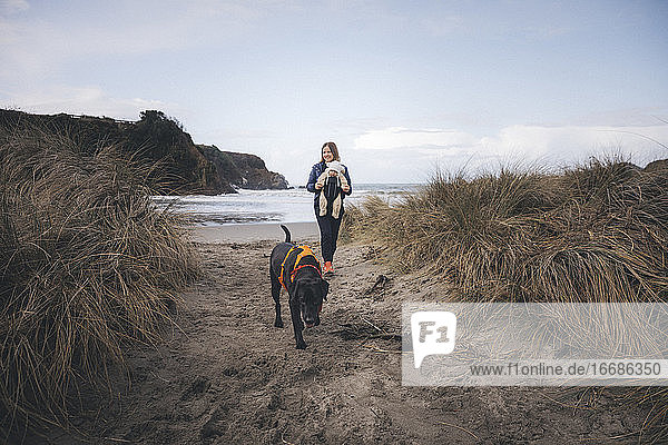 Eine Frau mit einem Kleinkind spielt mit einem Hund am kalifornischen Strand