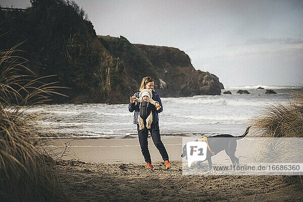 Eine Frau mit einem Kleinkind spielt mit einem Hund am kalifornischen Strand