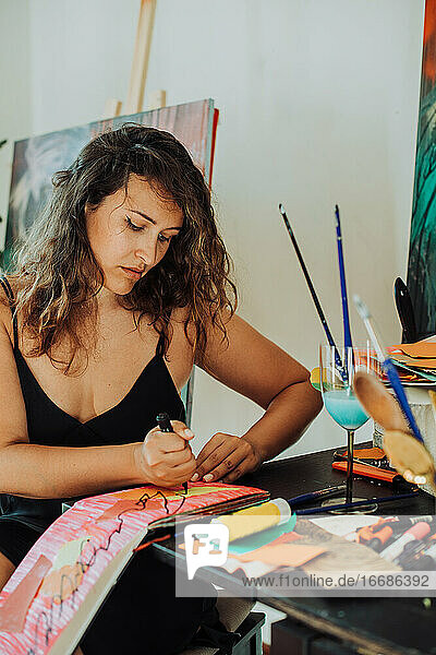 Malerin konzentriert auf die Arbeit sitzend am Tisch in ihrem Atelier  Nahaufnahme