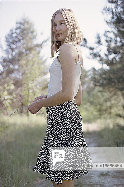 Blond woman in skirt standing by footpath in spring forest.