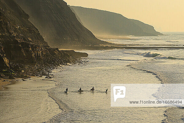 Gruppe von Surfern  die bei Sonnenuntergang auf dem Meer surfen.