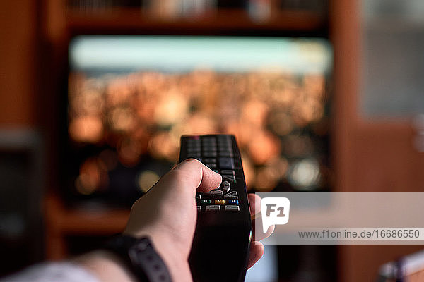 Close-up of a man changing channels with a remote control at home