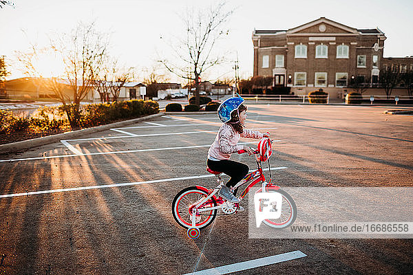 Junges Mädchen fährt auf einem Fahrrad mit Stützrädern auf einem leeren Parkplatz