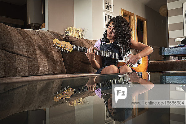 a little girl concentrating while playing guitar in the living room