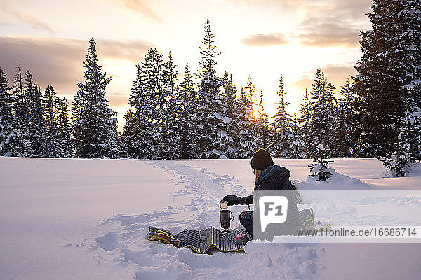 Female hiker preparing food on snow covered land during sunset