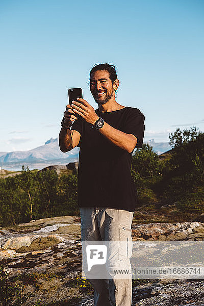 Man smiling taking a photo with his smartphone on top of a mountain