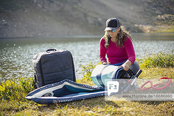 Woman unpacking paddleboard from backpack at lakeshore