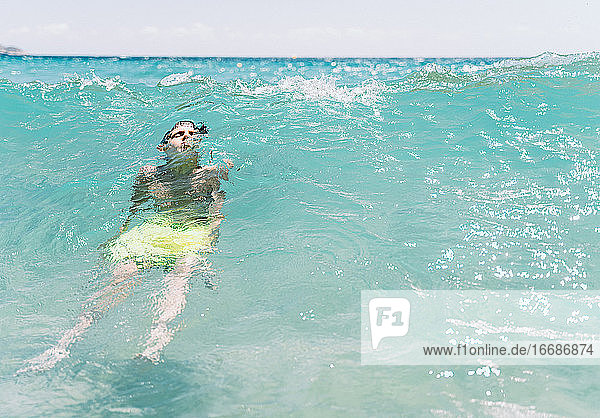 entspannter weißer Junge mit geschlossenen Augen  der im Sommer eine Welle im Meer taucht