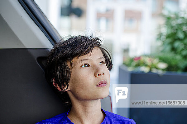 A young boy leans back in the trunk of a van looking up at the sky