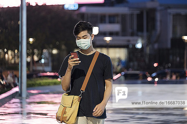 Young man with protective face mask using mobile phone in city s