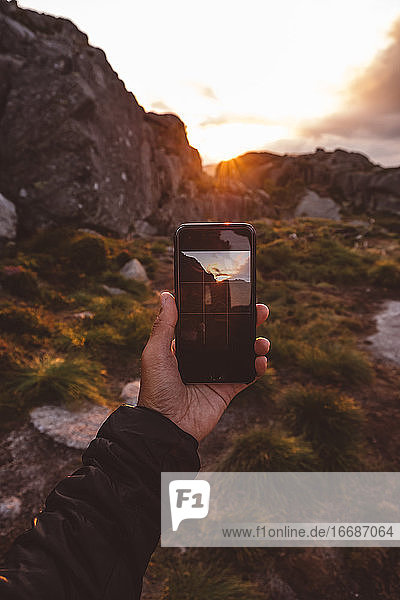 Eine Hand hält ein Smartphone mit einem Bild einer vom Sonnenuntergang beleuchteten Szene