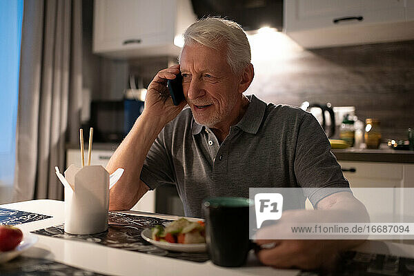 Älterer Mann spricht während des Abendessens mit seinem Smartphone