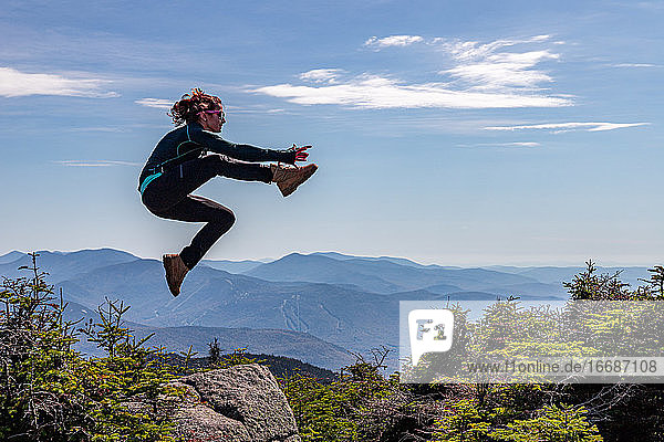 Junge Frau springt in den White Mountains von einem Felsen.
