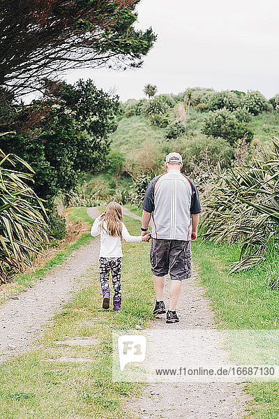 Father and daughter walking down scenic track holding hands