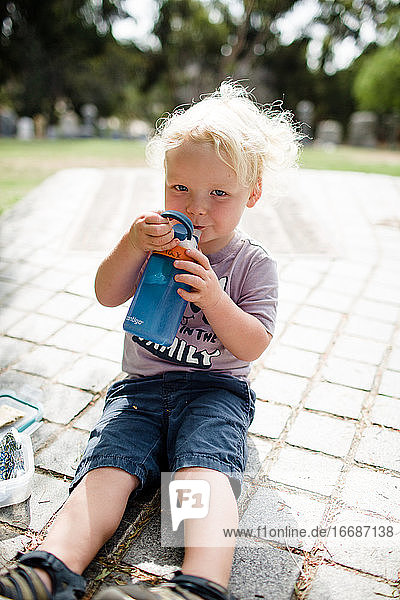 Zweijähriges Kind  das beim Trinken von Wasser in die Kamera grinst