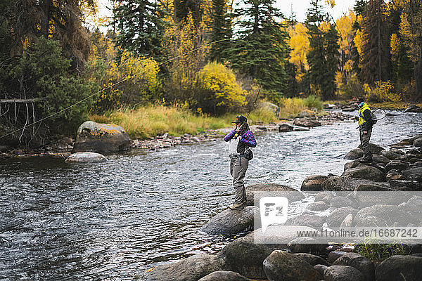 Man and woman fly fishing while standing on rocks at Roaring Fork River