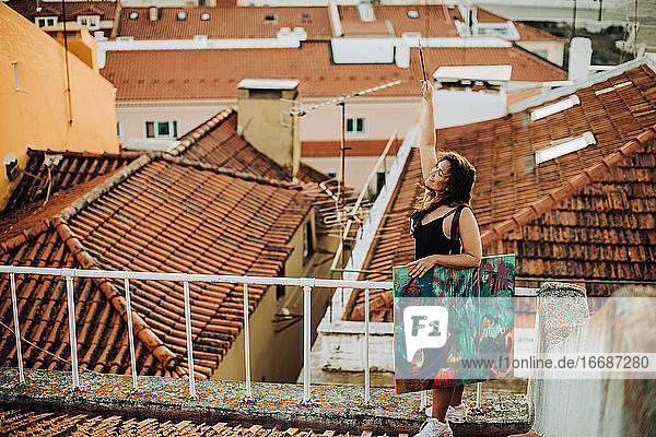 Unbeschwerte glückliche Frau mit Gemälde auf einem gekachelten Dach in Lissabon