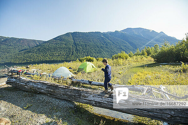 Young boy balancing on fallen log near wilderness campsite  Canada.