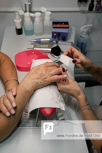 senior woman in cosmetic salon doing manicure with specialist