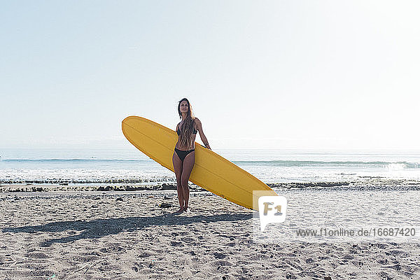 Porträt einer Surferin  die mit Longboard am Strand posiert