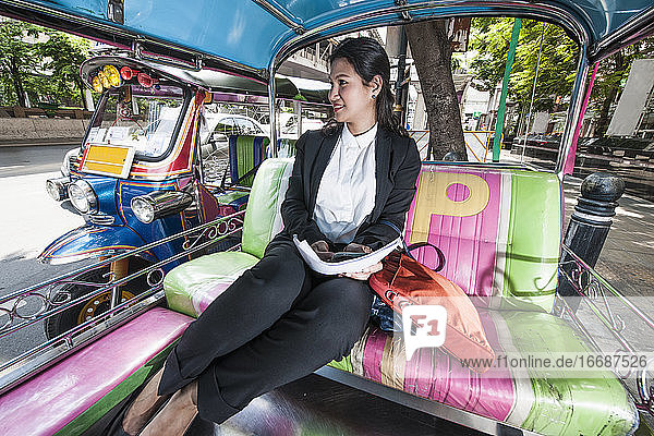 Geschäftsfrau bei der Arbeit auf der Rückbank eines traditionellen thailändischen Tuktuks