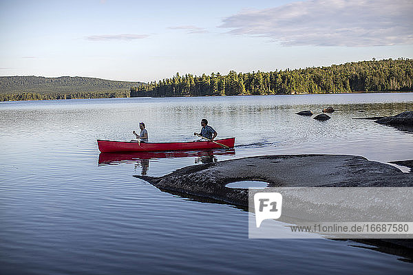 Paddler steuern ihr Kanu an einer felsigen Stelle auf einem See in der Wildnis in Maine vorbei