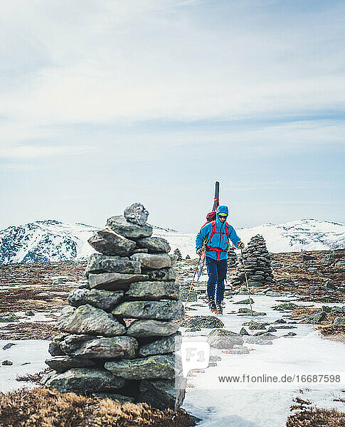 Man following cairns across snow and ice with skis on back