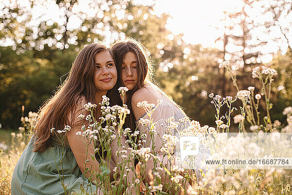 Portrait of two girlfriends sitting amidst flowers in summer forest