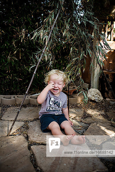 Zwei Jahre alter Junge unter Bambus sitzend und lachend