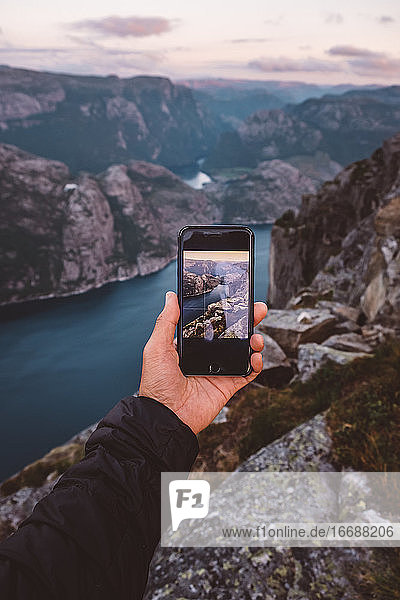 Hand hält Smartphone mit Bild der Szene im Hintergrund auf sie an norwegischen Fjorden