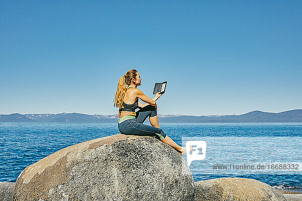 Junge Frau sitzt am Lake Tahoe und liest tagsüber ein Kindle-Buch