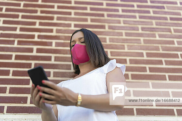 schöne Frau mit rosa Maske tippt eine Nachricht auf ihrem Smartphone