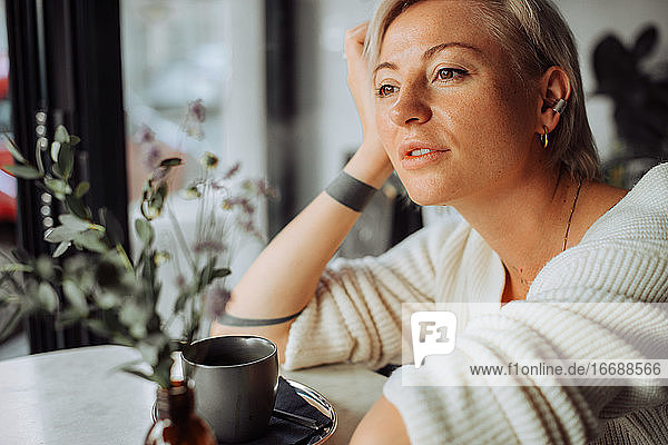 Blond woman sitting at table with cup of coffee looking at window