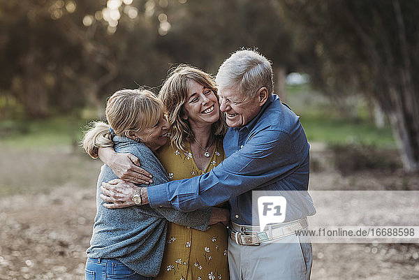Portrait of Adult Woman and Senior Parents Hugging at Park