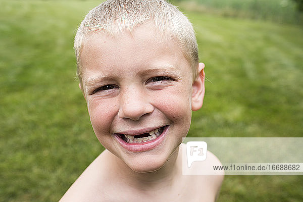 Nahaufnahme eines lächelnden zahnlosen Jungen mit einem Buzz Cut im Hinterhof