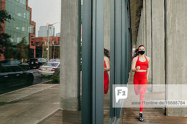 Junge Frau in roter Sportkleidung  die auf der Straße läuft und eine Gesichtsmaske trägt.